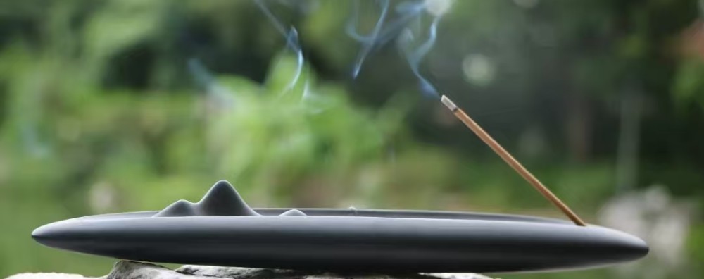 Burning incense stick with glowing ember and smoke in a ceramic holder